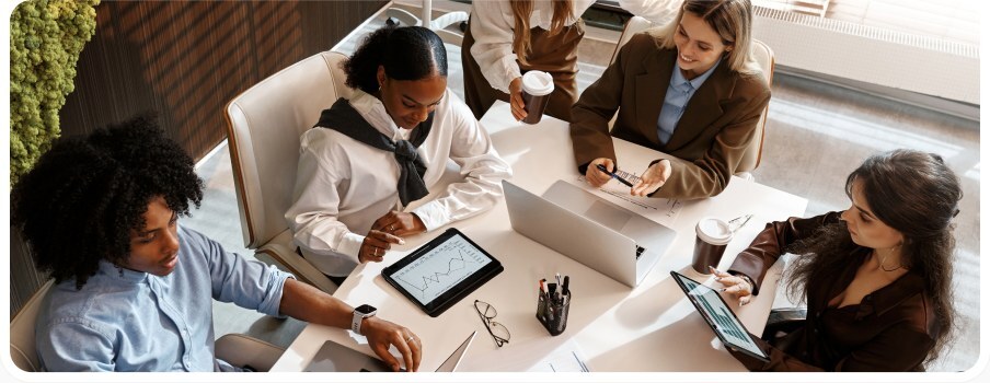 Five finance professionals working together around a table with laptops and a tablet