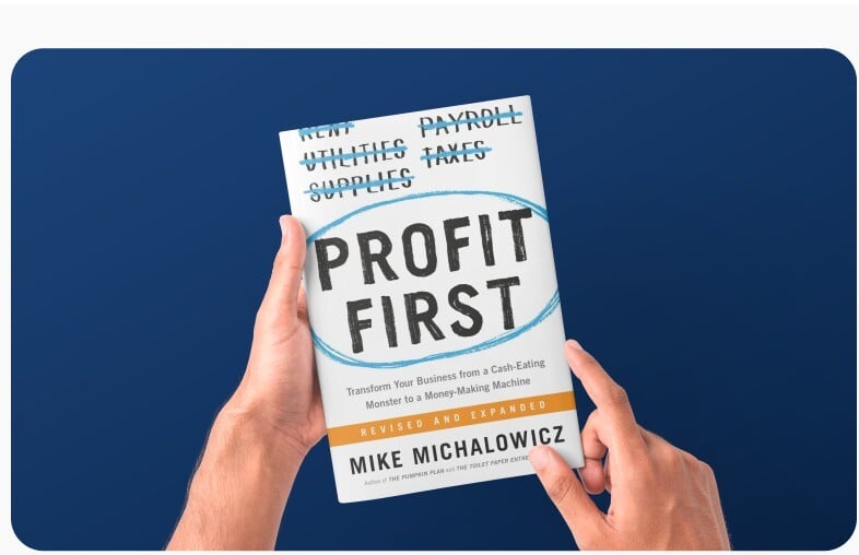 Hands holding a copy of Profit First against a navy background